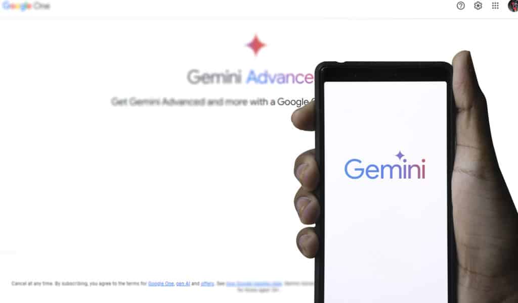 Hand holding a smartphone with the Gemini logo on-screen, with 'Gemini Advance' in the background.