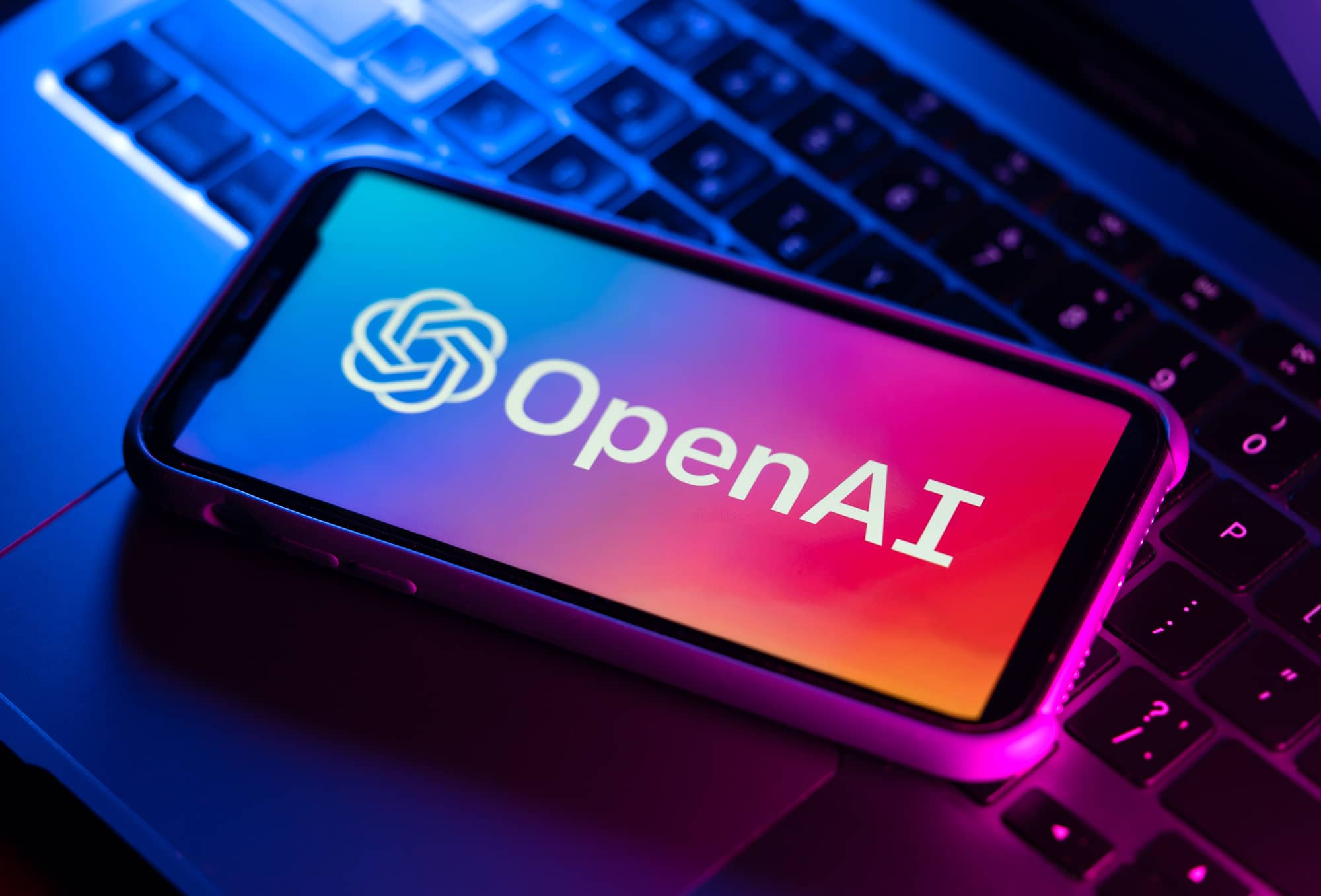 Smartphone with OpenAI logo displayed on the screen, placed on a laptop keyboard with purple backlighting, symbolizing advanced AI technology such as voice engine capabilities.