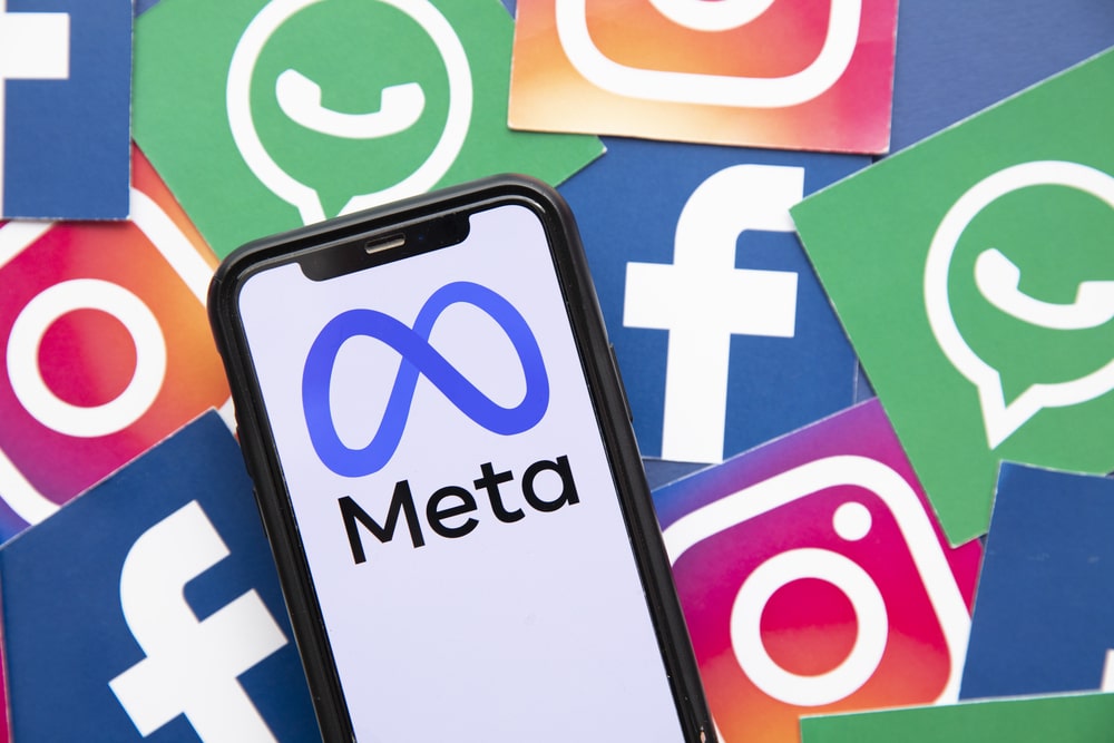 A smartphone screen displaying the Meta logo, flanked by the logos of Facebook, Instagram, and WhatsApp, illustrating the reach of Meta AI across social platforms.