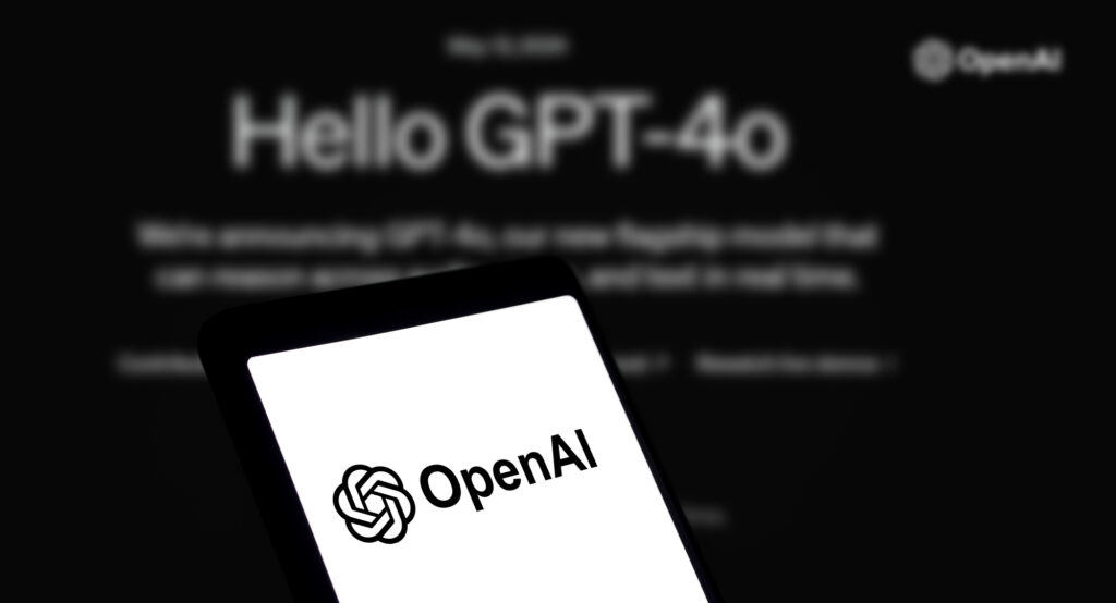 A close-up of a smartphone with the OpenAI logo displayed, with "Hello GPT-4o" in blurry text in the background.