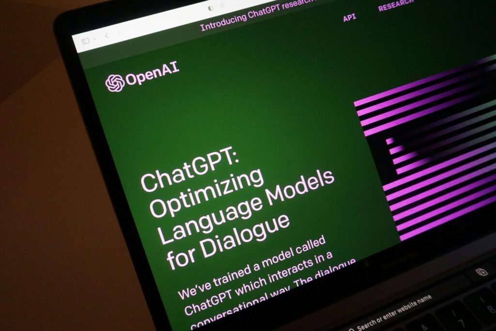 A laptop screen displays an OpenAI page about using ChatGPT to write and optimize dialogue in language models.