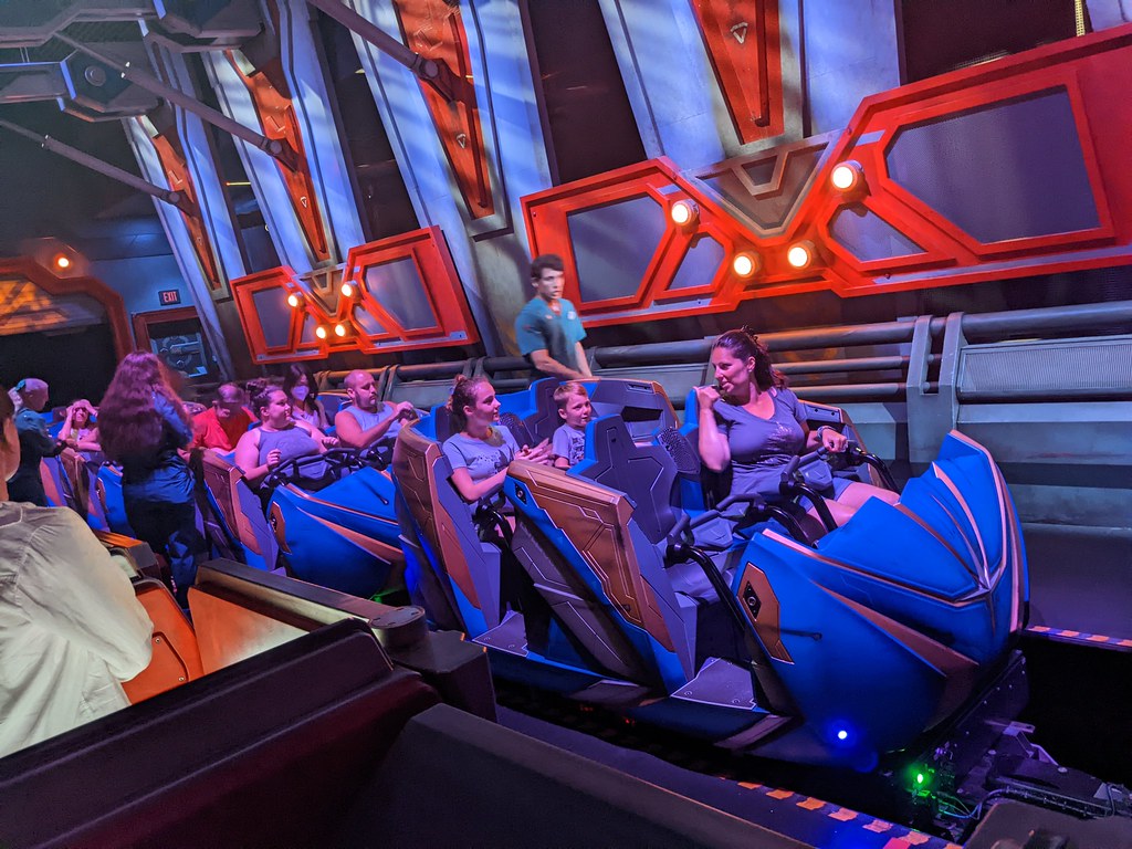 Guests seated on a futuristic Disney ride vehicle, surrounded by vibrant, high-tech interior design