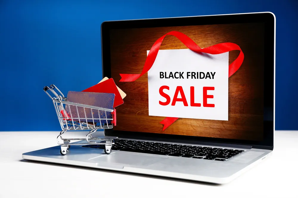 ai and black friday sale on a laptop screen with a mini shopping cart and credit cards on the keyboard