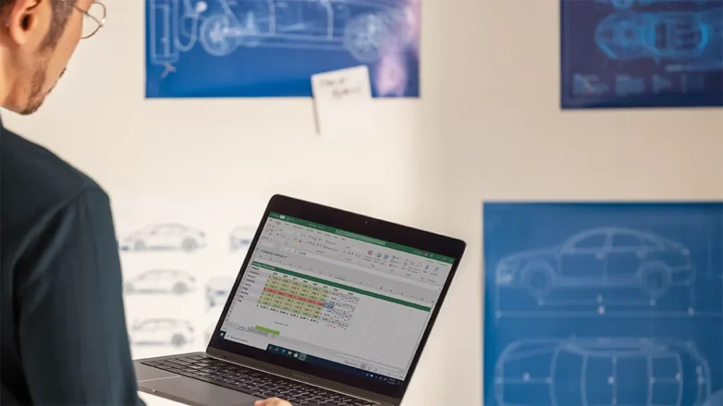 how to use microsoft copilot in Excel shown by a person reviewing a spreadsheet on a laptop in front of automotive design blueprints
