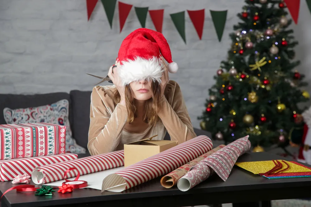 AI Christmas stress concept with a tired woman in a Santa hat sitting at a table covered in wrapping paper and gifts