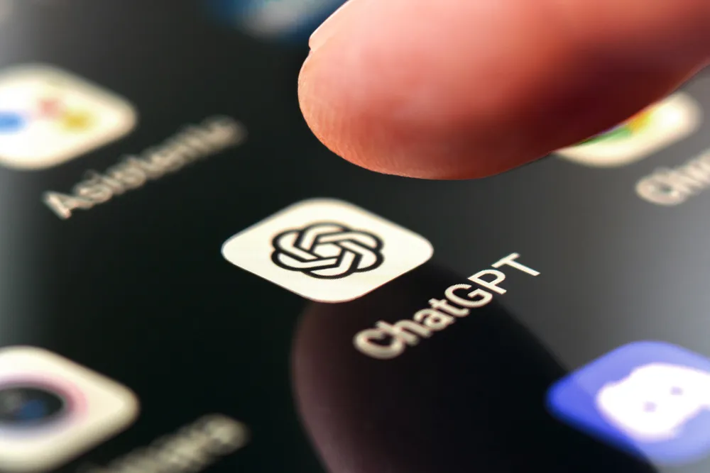 A finger tapping the ChatGPT app icon on a smartphone screen, shown alongside Alexa+ as part of a comparison between leading AI assistants.